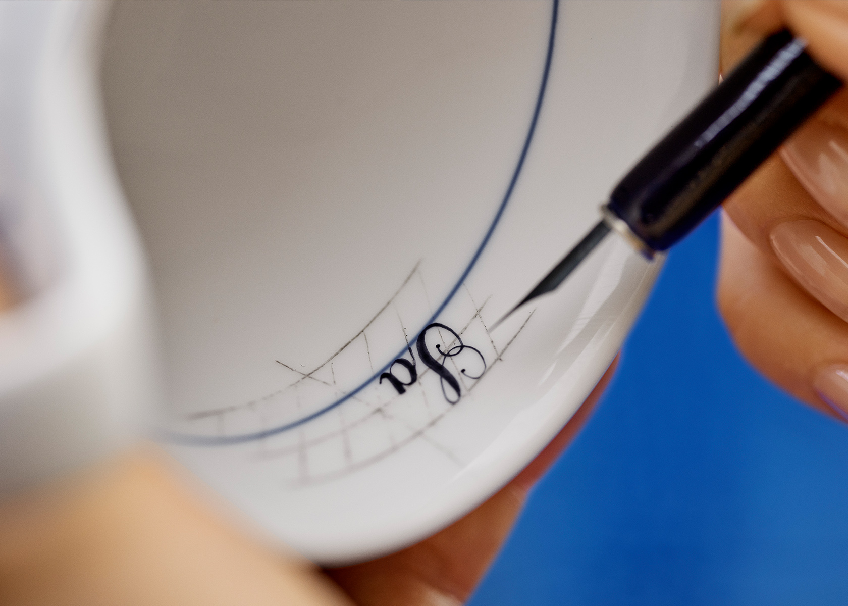 A close up of how a Royal Copenhagen painter is painting the name on the inside of a cup upside down